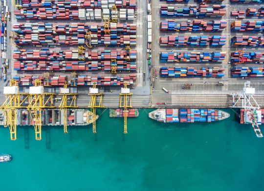 container ship in import export and business logistic.By crane , Trade Port , Shipping.Tugboat assisting cargo to harbor.Aerial view.